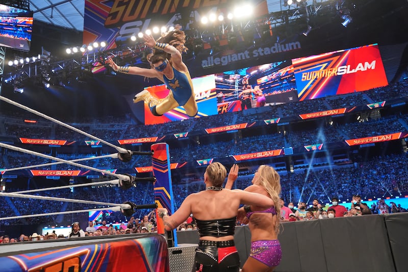 Nikki ASH dives from the top rope to her opponents Rhea Ripley and Charlotte Flair. Photo: WWE