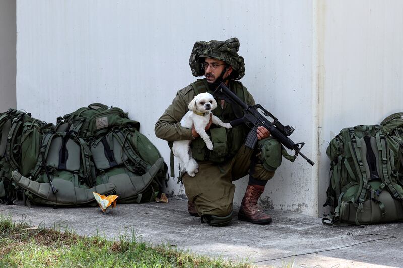 An Israeli soldier holds a rescued dog as he takes position near a bomb shelter in Kibbutz Kfar Aza, southern Israel. Reuters