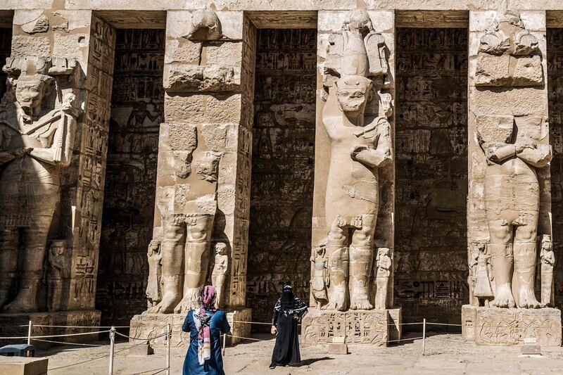 Tourists pose for pictures before gigantic statues at the Mortuary Temple of Ramesses III near Luxor. AFP