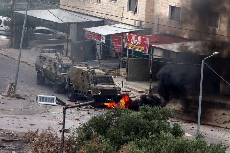 Tyres burn beneath Israeli security forces armoured vehicles during a raid in Jenin. AP