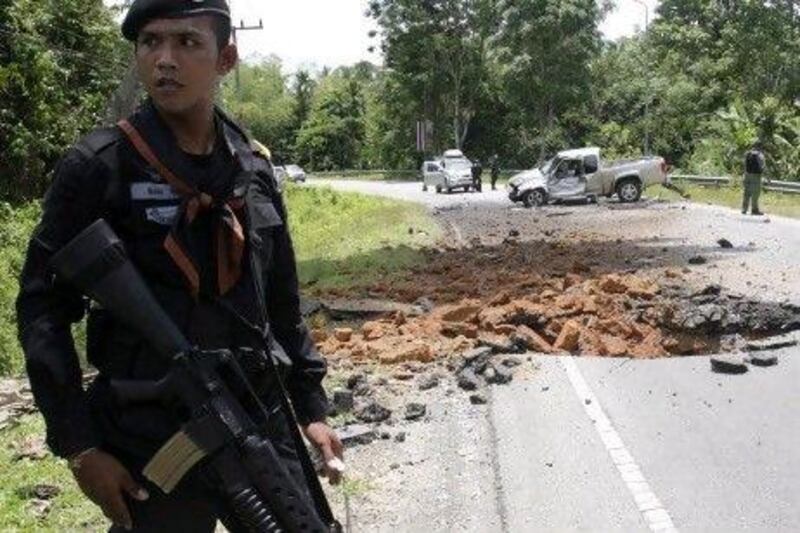 A Thai paramilitary ranger patrols the road while a bomb disposal unit inspects a damaged lorry following a roadside bomb attack in Narathiwat province, southern Thailand on Friday. The Thai government is to compensate families of those killed in the conflict, which started in 2004.