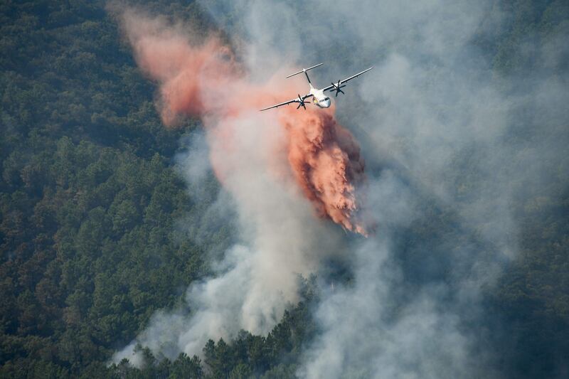 A firefighting plane drops fire retardant on to a smoking forest in the hillside near Grimaud.
