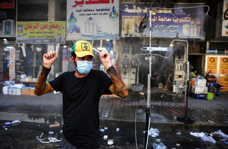 A man clad in mask due to the COVID-19 coronavirus pandemic stands next to sprinklers along Sinak street in Iraq's capital Baghdad on August 9, 2020, to cool off due to extremely high temperature rises amidst a heatwave.  / AFP / AHMAD AL-RUBAYE
