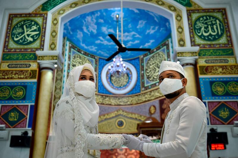 A couple wearing face masks amid the COVID-19 coronavirus attends to their wedding ceremony at a mosque in Banda Aceh on June 3, 2020. / AFP / CHAIDEER MAHYUDDIN
