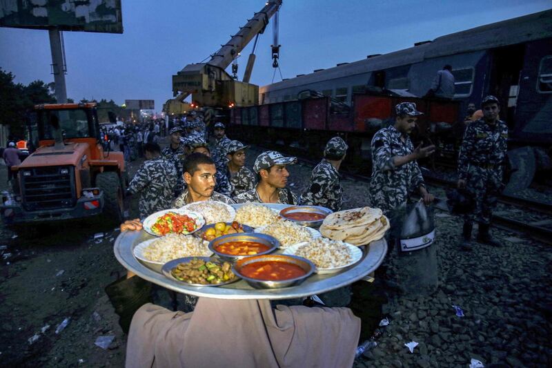 A woman carries a tray loaded with food, for people to break their Ramadan fast, as she walks towards Egyptian security forces standing guard near a telescopic railway crane lifting an overturned passenger carriage at the scene of a railway accident in the city of Toukh in Egypt's central Nile Delta province of Qalyubiya. AFP