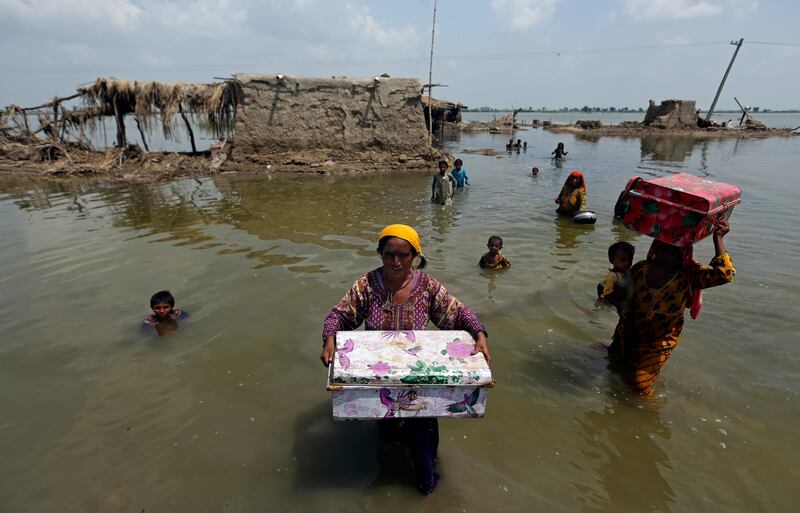 Women carry belongings salvaged from their flooded home after monsoon rains, in the Qambar Shahdadkot district of Sindh Province in Pakistan in September 2022. AP Photo