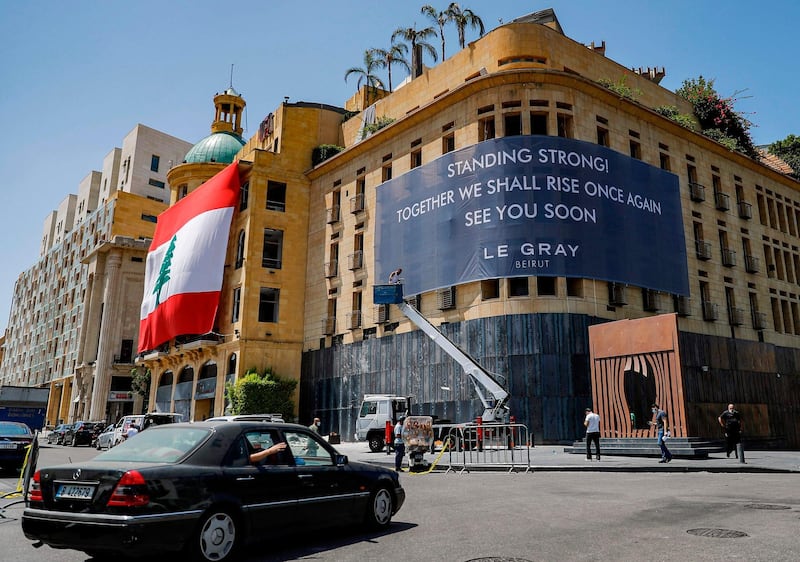 This picture taken on August 19, 2020 shows a view of the landmark Le Gray hotel in the centre of Lebanon's capital Beirut overlooking the Martyrs' Square, as a banner is hung across its facade reading in English "Stay strong! Together we shall riise once again, see you soon", and a giant Lebanese national flag hung over the facade of the neighbouring building, in the aftermath of the monster blast that ravaged the city earlier in August.  / AFP / JOSEPH EID
