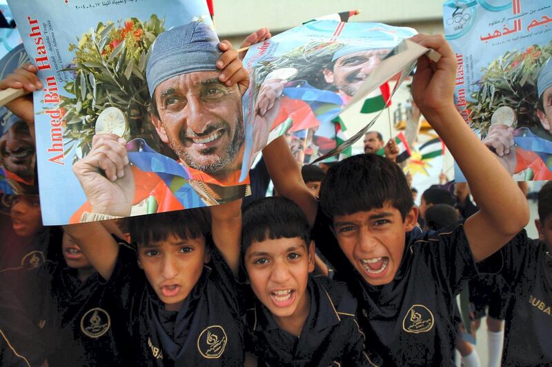 Emirati boys hold up 26 August 2004 pictures of Sheikh Ahmed bin Hashr Al-Maktoum, who arrived in his country after winning a historic first gold medal during the Athens Olympics in the men's double trap shooting. Al-Maktoum became the first athlete from the UAE to win an Olympic medal of any colour with a superb display of shooting at the Markopoulo Shooting Centre in Athens. AFP PHOTO/Nasser YOUNES (Photo by NASSER YOUNES / AFP)