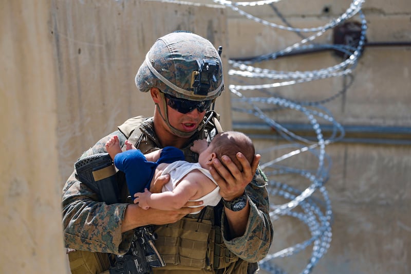 A US Marine comforts an infant while they wait for the mother during an evacuation at Hamid Karzai International Airport on August 21, 2021. Reuters