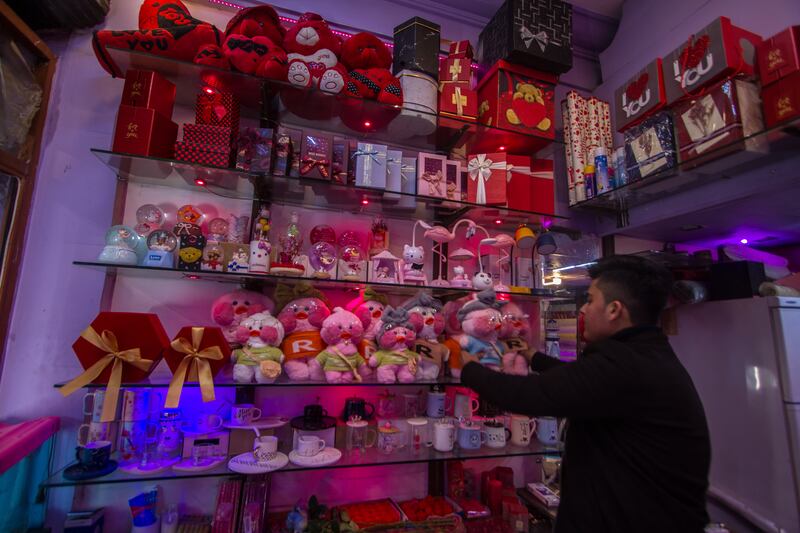 A gift shop owner arranges red gifts on the shelves inside his shop.