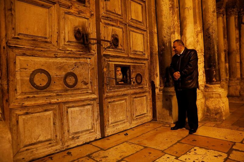 Adeeb Joudeh (R), a Muslim, who says his family were entrusted as the custodians of the ancient key to the Church of the Holy Sepulchre, looks at a priest as he peers through an opening in the church doors as they prepare to open it, in Jerusalem's Old City November 3, 2017. Picture taken November 3, 2017. REUTERS/Ronen Zvulun - RC1DD02C3200