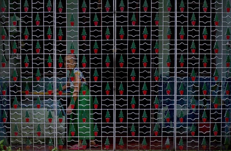 A woman stands in her veranda behind an iron-grill, speckled with Christmas trees in Yangon, Myanmar. Gemunu Amarasinghe / AP Photo