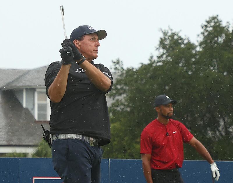 Phil Mickelson plays his shot from the first tee as Tiger Woods looks on. Getty