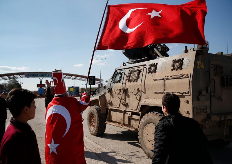 In support of the Turkish forces' offensive, codenamed 'Olive Branch' in the Kurdish-controlled enclave of Afrin, Syria, Isikli Tosun Baba, 60, dressed in a Turkish flag, waves one as a Turkish forces armoured personnel carrier is driven past, at the Oncupinar border crossing with Syria, known as Bab al Salameh in Arabic, in the outskirts of the town of Kilis, Sunday, Jan. 28, 2018. (AP Photo/Lefteris Pitarakis)