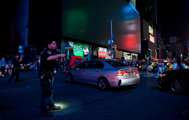 A police officer directs traffic with Times Square's dark billboards in the background after a power outage hit Manhattan in New York City.  AFP