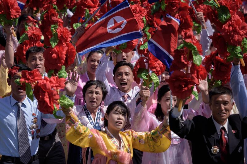 Participants wave flowers as they march past a balcony from where North Korea's leader Kim Jong Un was watching, during a mass rally on Kim Il Sung square in Pyongyang.  AFP