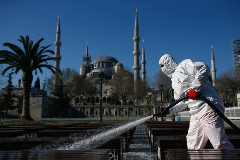 A municipality worker wearing a face mask and protective suits disinfects chairs outside the the historical Sultan Ahmed Mosque, also known as Blue Mosque, amid the coronavirus outbreak, in Istanbul, Saturday, March 21, 2020.  The new COVID-19 coronavirus can cause mild or moderate symptoms, but for some it can cause severe illness. (AP Photo/Emrah Gurel)