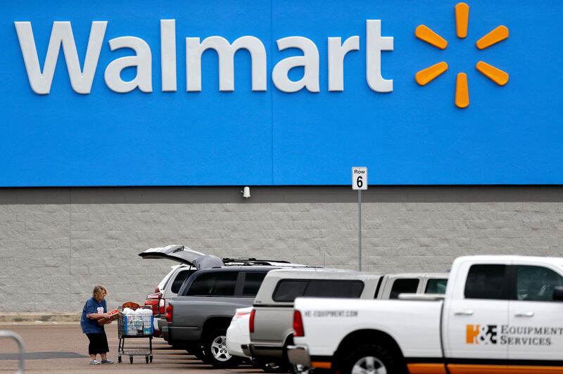 FILE - In this March 31, 2020 file photo, a woman pulls groceries from a cart to her vehicle outside of a Walmart store in Pearl, Miss. Walmart will require customers to wear face coverings at all of its namesake and Sam's Club stores. The company said the policy will go into effect on Monday, July 20, 2020 to allow time to inform stores and customers. (AP Photo/Julio Cortez, File)