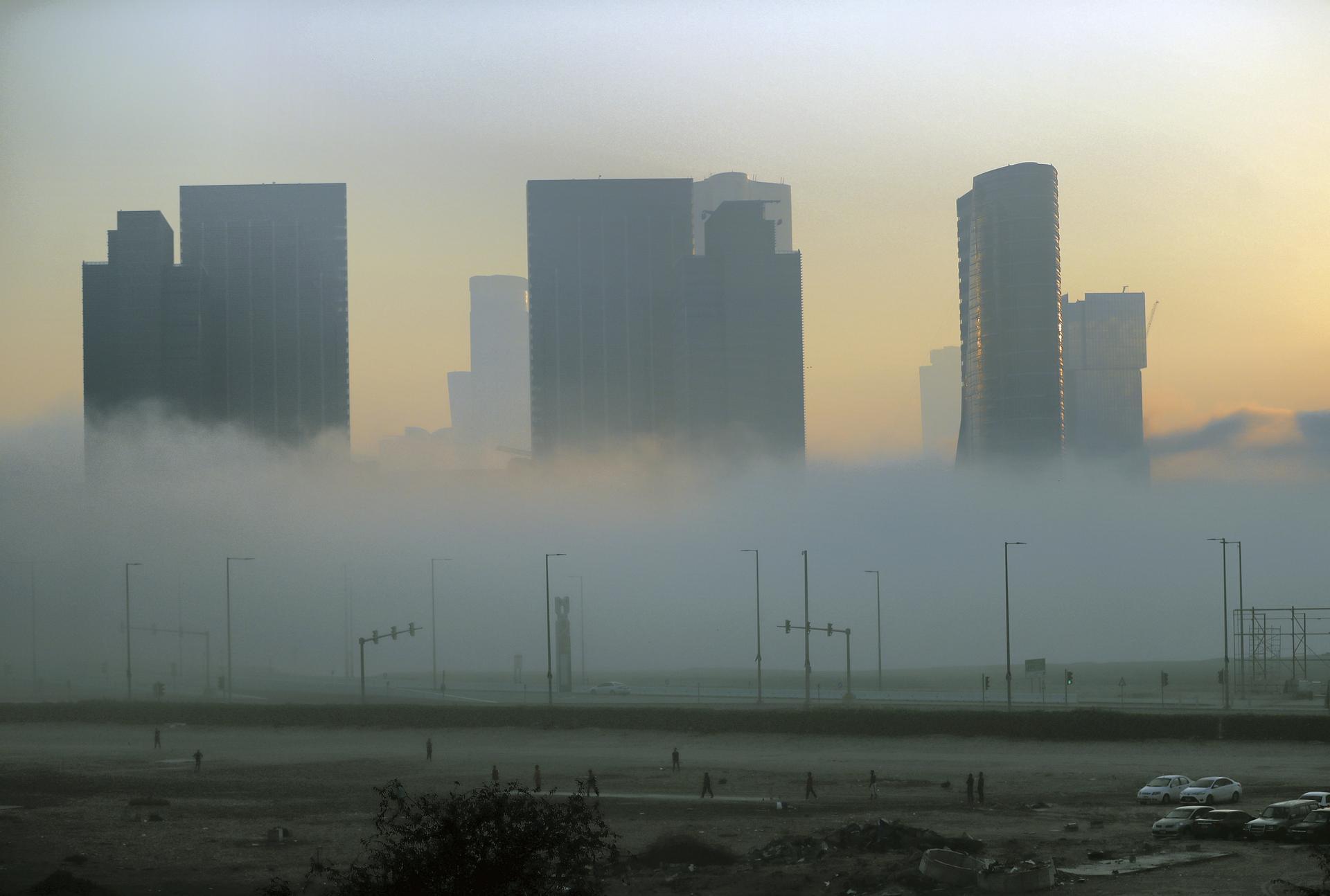 Abu Dhabi - United Arab Emirates - 22Dec2017 - Residence playing cricket in the foreground in tourist club area as dense fog engulfed Abu Dhabi city in the morning having poor visibilty for motorist. Ravindranath K / The National