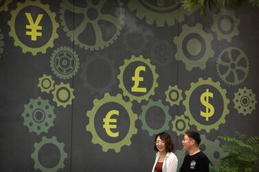 People walk past a mural showing symbols of world currencies in Beijing. The US-China trade war has crimped the global economy's growth, according to the World Bank and IMF, and its reverberations are affecting energy markets and economies of the Middle East and North Africa. AP