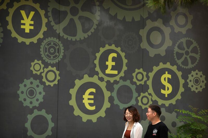 People walk past a mural on a bank showing symbols for American, Chinese and other world currencies in Beijing, Saturday, July 7, 2018. The trade war that erupted Friday between the U.S. and China carries a major risk of escalation that could weaken investment, depress spending, unsettle financial markets and slow the global economy. China's currency, has dropped against the dollar over the past month, giving Chinese companies a price edge over their U.S. competition. The drop might reflect a deliberate devaluation by Beijing, according to a banking trade group. (AP Photo/Mark Schiefelbein)