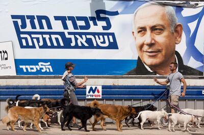 Dog walkers argue as they pass by an election campaign billboard shows Israeli Prime Minister Benjamin Netanyahu in Tel Aviv, Israel, Monday, April 8, 2019. Israel's election on Tuesday boils down to a referendum on Prime Minister Benjamin Netanyahu, who has dominated the country's politics for the better part of three decades. The Hebrew writing say "Strong Likud, Strong Israel. (AP Photo/Ariel Schalit)