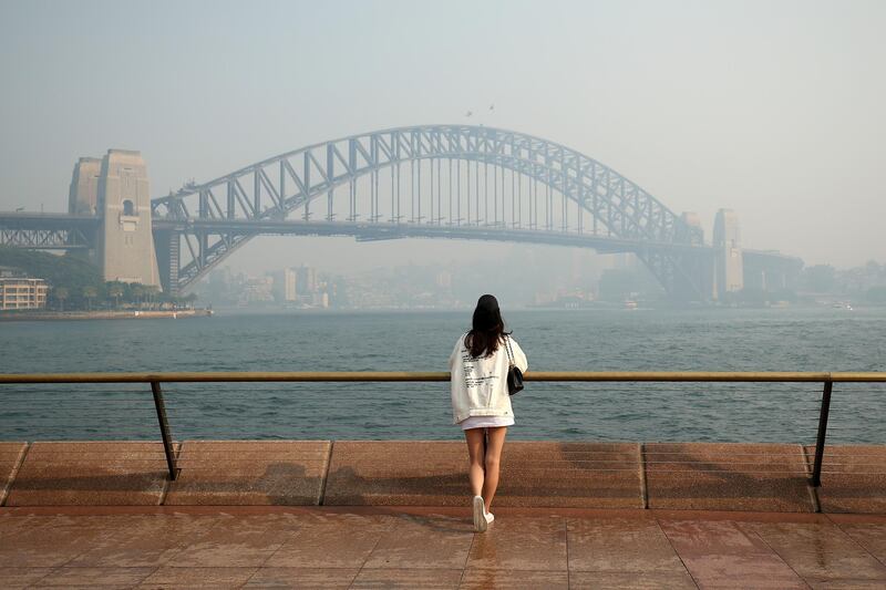 A woman looks at the Sydney Harbour Bridge and central business district shrouded in haze. Bloomberg