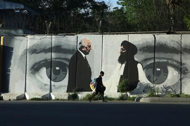 A young boy walks past a mural in Kabul depicting US peace envoy Zalmay Khalilzad and senior Taliban negotiator Abdul Ghani Baradar. AP Photo