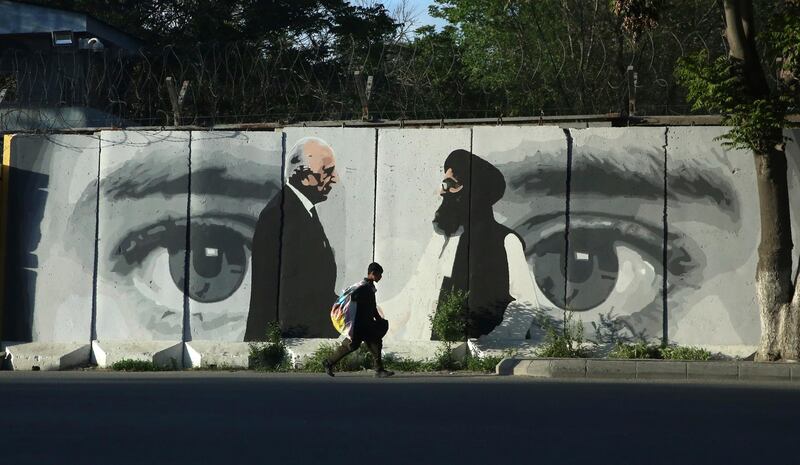 A young boy carries a sack of goods on his back walks past a wall depicting Washington's peace envoy Zalmay Khalilzad, left,  and Mullah Abdul Ghani Baradar, the leader of the Taliban delegation, in Kabul, Afghanistan, Tuesday, May 4, 2020. (AP Photo/Rahmat Gul)