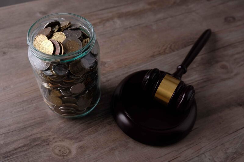 High Angle View Of Coins In Glass Of Jar On Table With Gavel. Getty Images