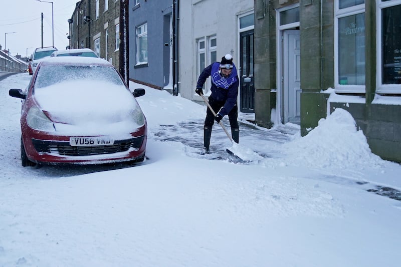 A man clears snow from the pavement in Tow Law, Co Durham. PA