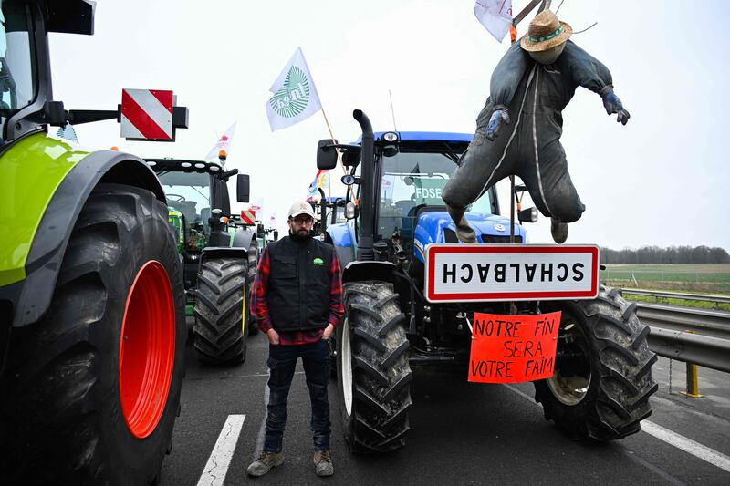 A farmer poses next to a tractor displaying a banner which reads as "Our end will be your hunger", as farmers coming from Meuse and Moselle block the A4 motorway near Jossigny, east of Paris. AFP