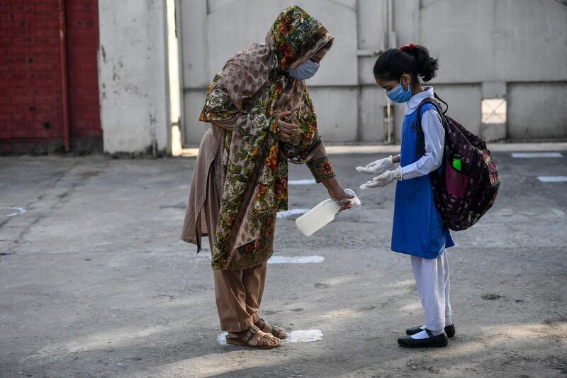 A teacher sprays disinfectant on the shoes of a child at the entrance of a junior campus school upon arrival in Islamabad. AFP