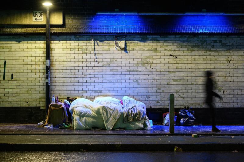 Commuters walk past three homeless people as they sleep in a thrown away bed underneath a railway bridge.  Leon Neal / Getty Images