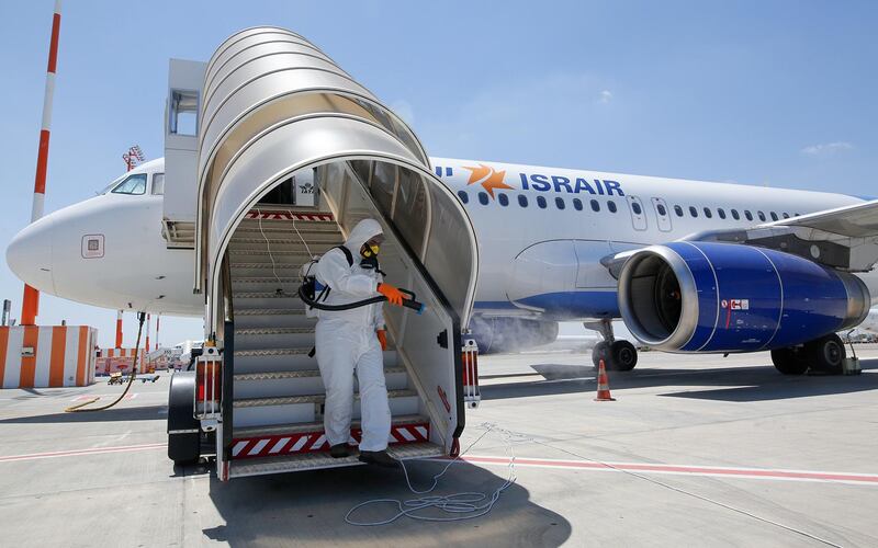 An Israeli worker in full hazmat suit sprays disinfectant on the boarding stairs of an Israir Airlines Airbus A320 airplane, at the Ben Gurion International Airport near the central Israeli city of Tel Aviv, on June 14, 2020, amid the novel coronavirus pandemic. (Photo by GIL COHEN-MAGEN / AFP)