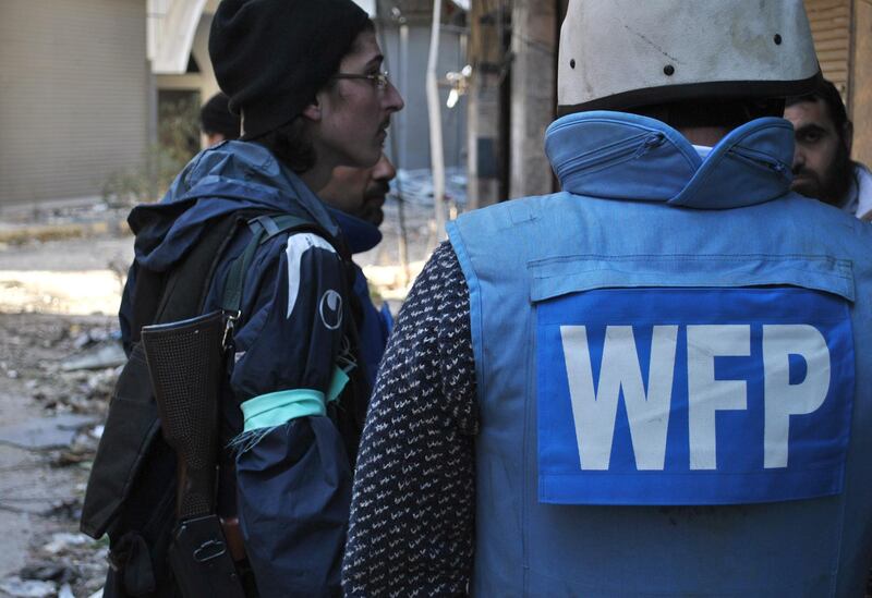 An United Nations World Food Programme (WFP) worker (R) talks with rebel fighters on February 8, 2014 on the second day of a humanitarian mission in a besieged district of the central city of Homs. The Syrian Red Crescent delivered a first batch of much-needed aid to civilians trapped for nearly two years in rebel-held areas of Homs city, despite coming under fire from mortars.  AFP PHOTO / BASSEL TAWIL (Photo by BASSEL TAWIL / BASSEL TAWIL / AFP)