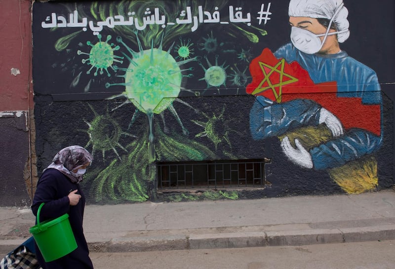 A woman walks past writing on a wall that encourages people to stay at home to prevent the spread of coronavirus, in Sale, Morocco. EPA