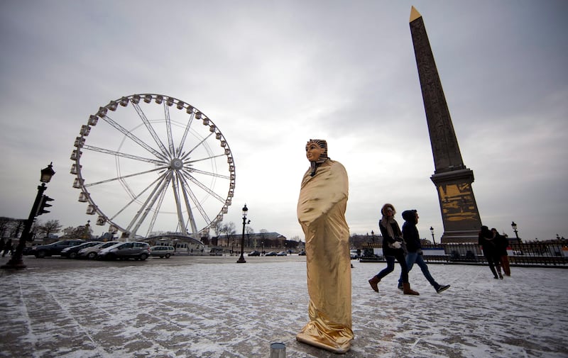 epa03093071 A street artist dresses as an Egyptian pharaoh (C) braves the cold as he performs in the snow on Place de la Concorde in Paris, France, as sub-freezing winter temperatures continue in Europe on 05 February 2012.  EPA/IAN LANGSDON *** Local Caption ***  03093071.jpg