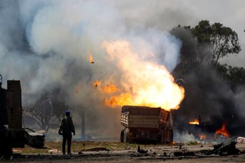 A rebel fighter looks at burning vehicles belonging to forces loyal to Libyan leader Muammar Gaddafi after an air strike by coalition forces, along a road between Benghazi and Ajdabiyah March 20, 2011. REUTERS/Goran Tomasevic (LIBYA - Tags: POLITICS CIVIL UNREST)