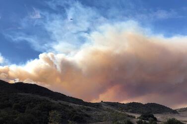 An airplane flies over a large wildfire plume from a recent flare-up of the Woolsey Fire near Lake Sherwood, California. AP