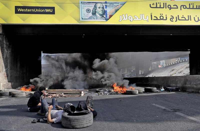 Anti-government protesters sit next to burning tyres at a makeshift roadblock in Zouk Mosbeh, north of Lebanon's capital Beirut. AFP