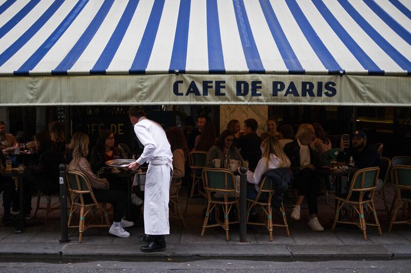 A waiter serves customers eating and drinking on the terrace area outside Cafe de Paris, ahead of the enforcement of new Covid-19 restrictions which will see bars and restaurants closing early, in Paris, France, on Monday, Sept. 28, 2020. President Emmanuel Macrons government is seeking to ease tension after the first significant tightening of restrictions on French daily life since the end of the lockdown in May. Photographer: Nathan Laine/Bloomberg