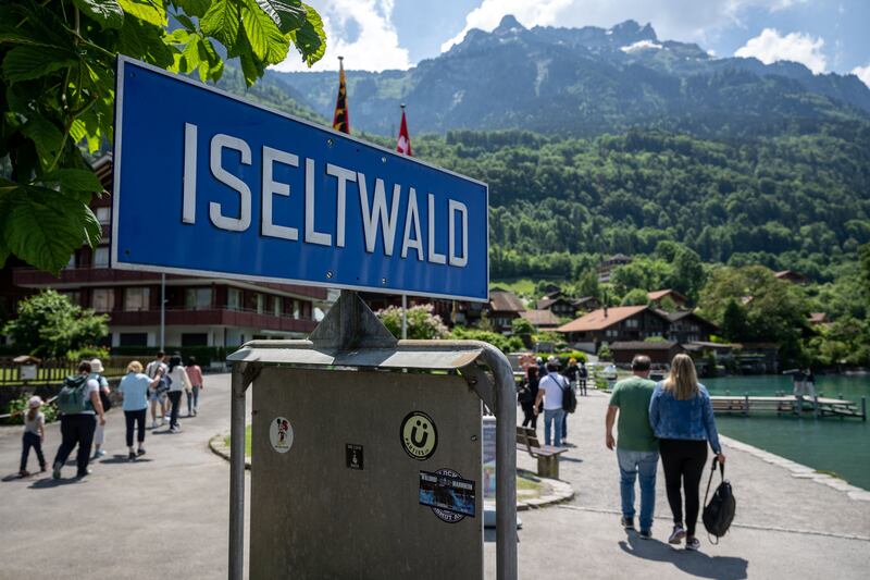 Tourists walk past a sign of Iseltwald 