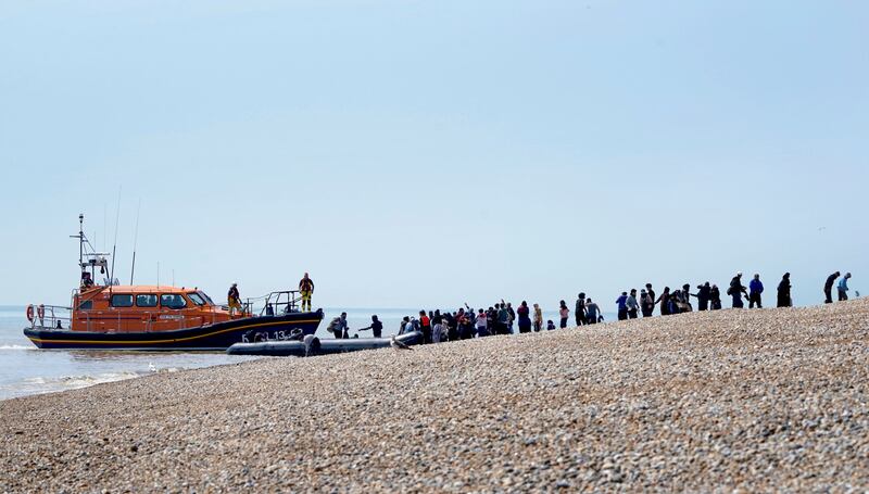 People thought to be migrants are watched over by the RNLI as they make their way up the beach after arriving on a small boat at Dungeness in Kent, England, July 19. AP