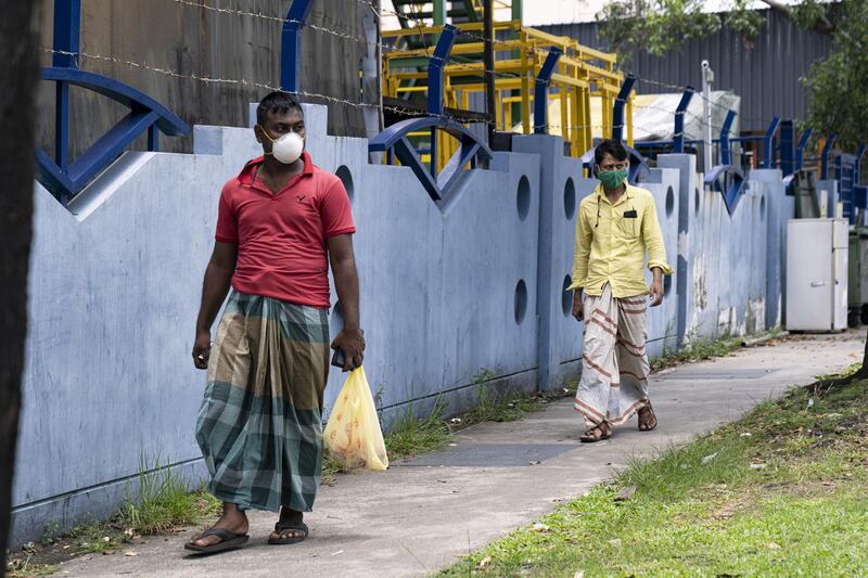 SINGAPORE - APRIL 20: Migrant workers wearing protective face masks walk past a factory-converted dormitory for migrant workers on April 20, 2020 in Singapore. Migrant workers in the construction industry have been served with a 14-day stay home notice starting from April 20th in order to curb the transmission of the coronavirus at work sites. (Photo by Ore Huiying/Getty Images)