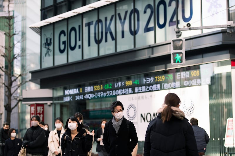People wearing face masks walk by Olympics-themed signs supported by a securities firm in Tokyo on Friday, Jan. 29, 2021. The postponed Tokyo 2020 Olympic games were rescheduled to be held in this summer. (AP Photo/Hiro Komae)