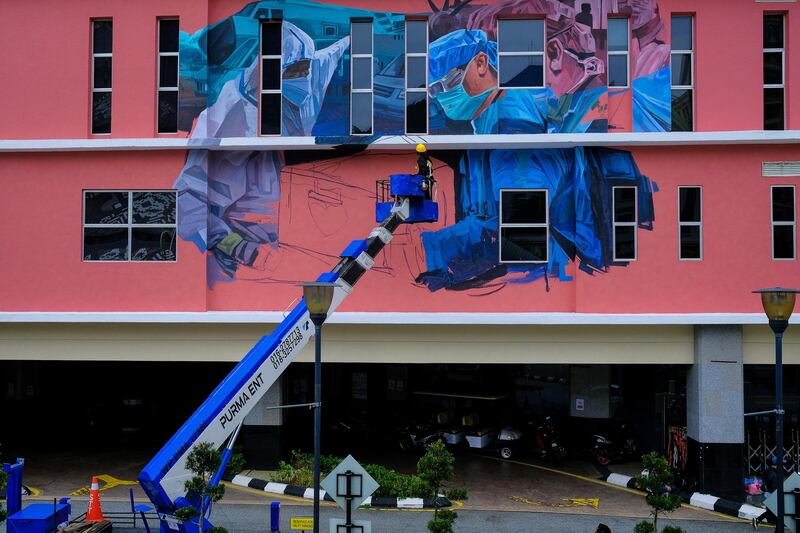 A worker standing on a crane platform paints a mural of health workers on the facade of the National Heart Institute in Kuala Lumpur, Malaysia.  Bloomberg
