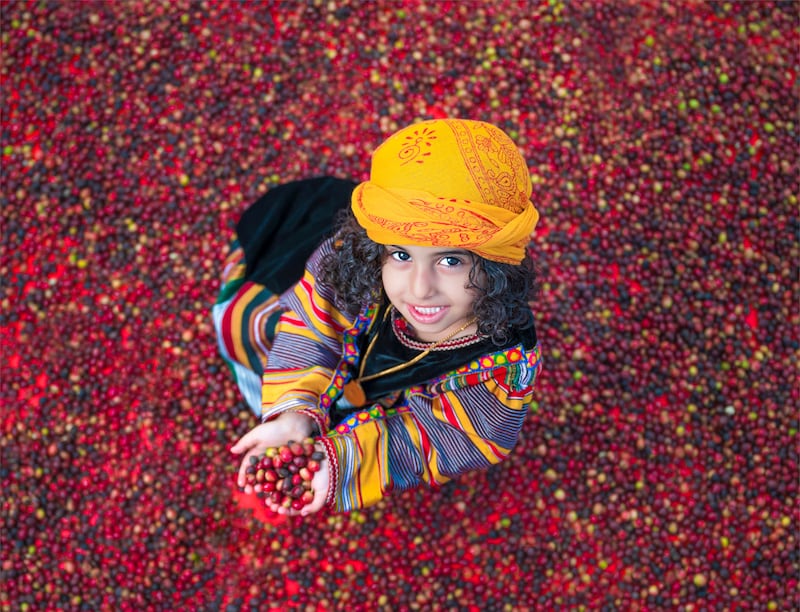 A child smiling as they hold up a handful of freshly picked coffee beans. Photo: Ministry of Culture