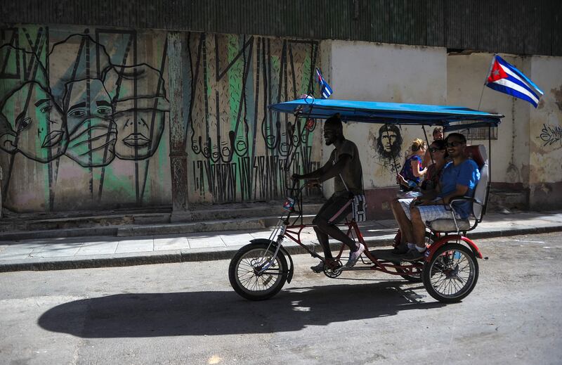 A rickshaw passes by a graffiti of street art in Havana.