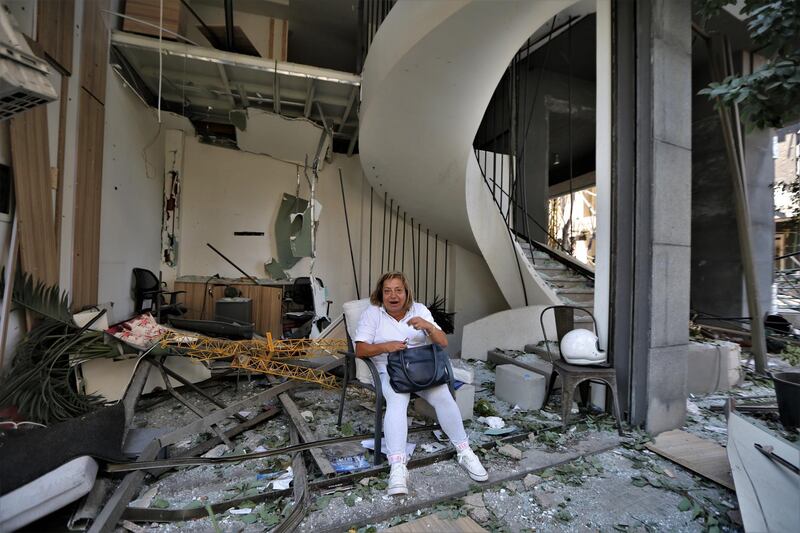 A woman sits in front of a damaged building.  EPA